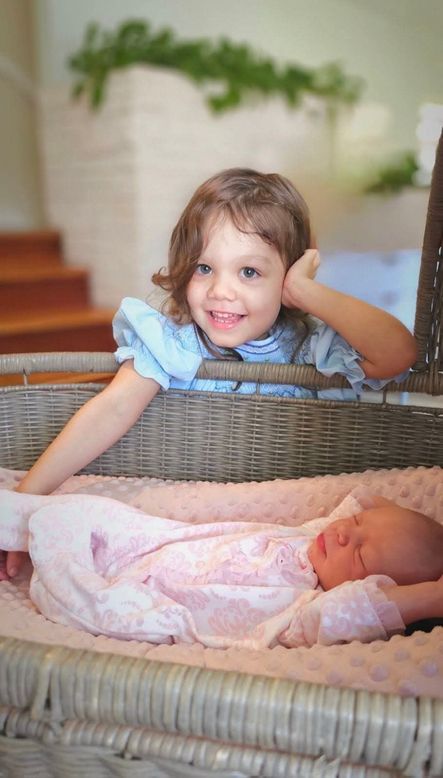 Big sister peeking at her newborn sister in a bassinet