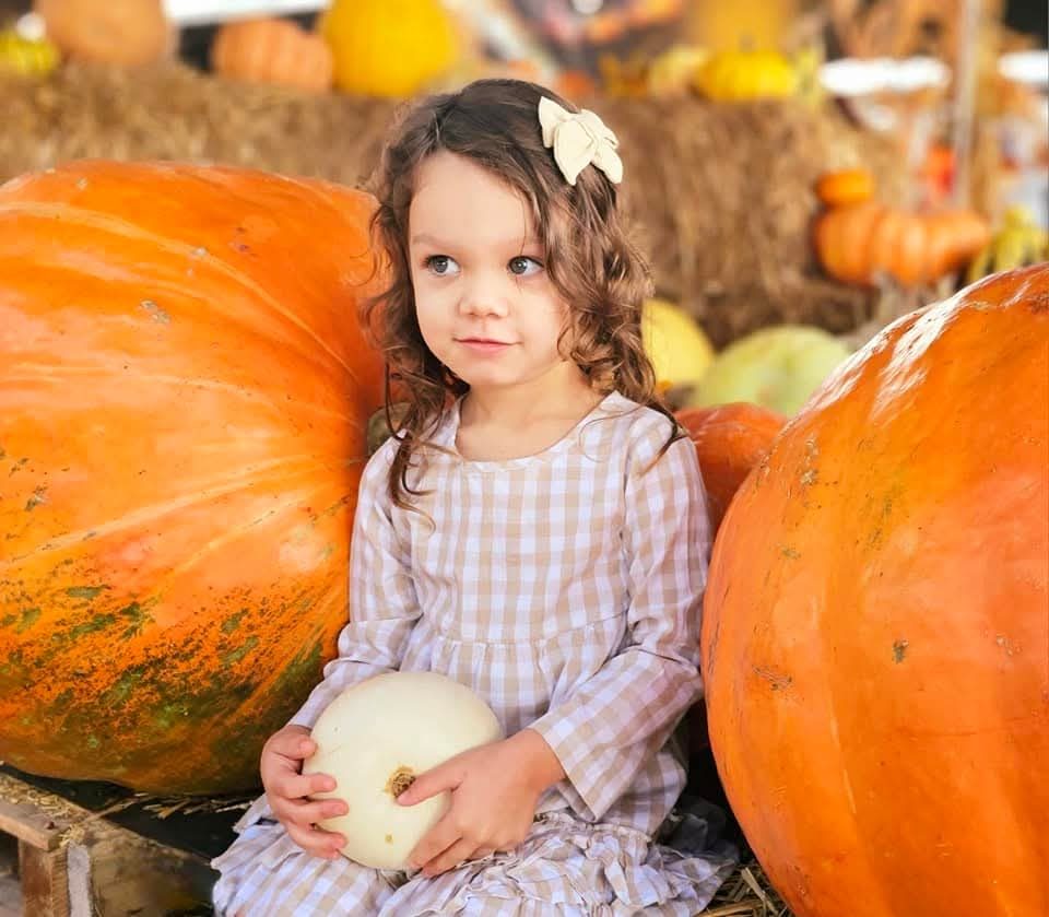 Girl in gingham sitting between giant pumpkins