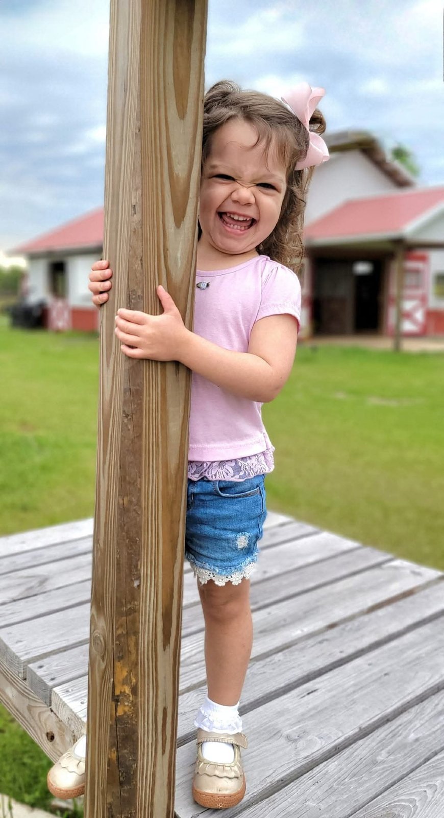 Toddler laughing while hugging a wooden post at a farm