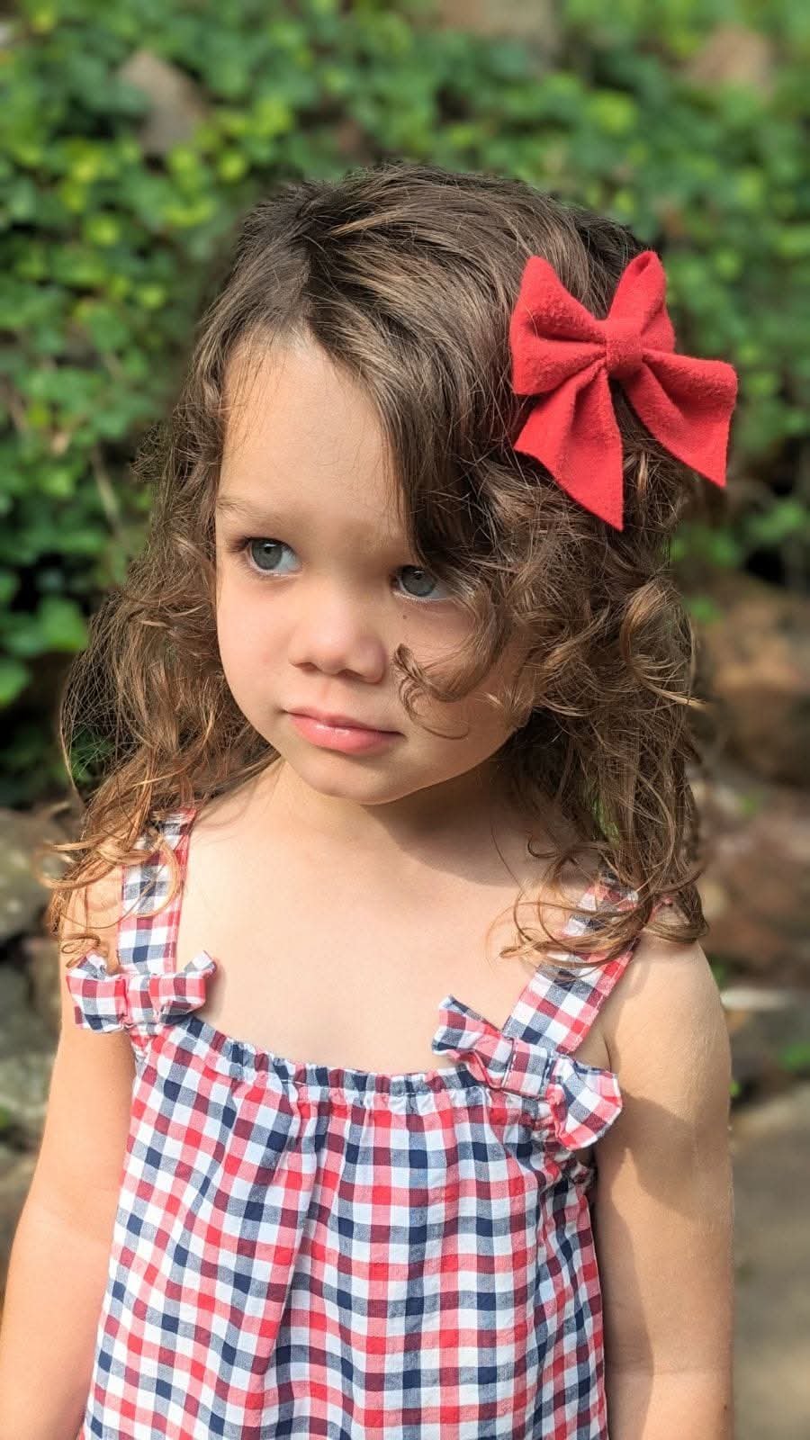 Girl in red gingham with a red bow, looking away