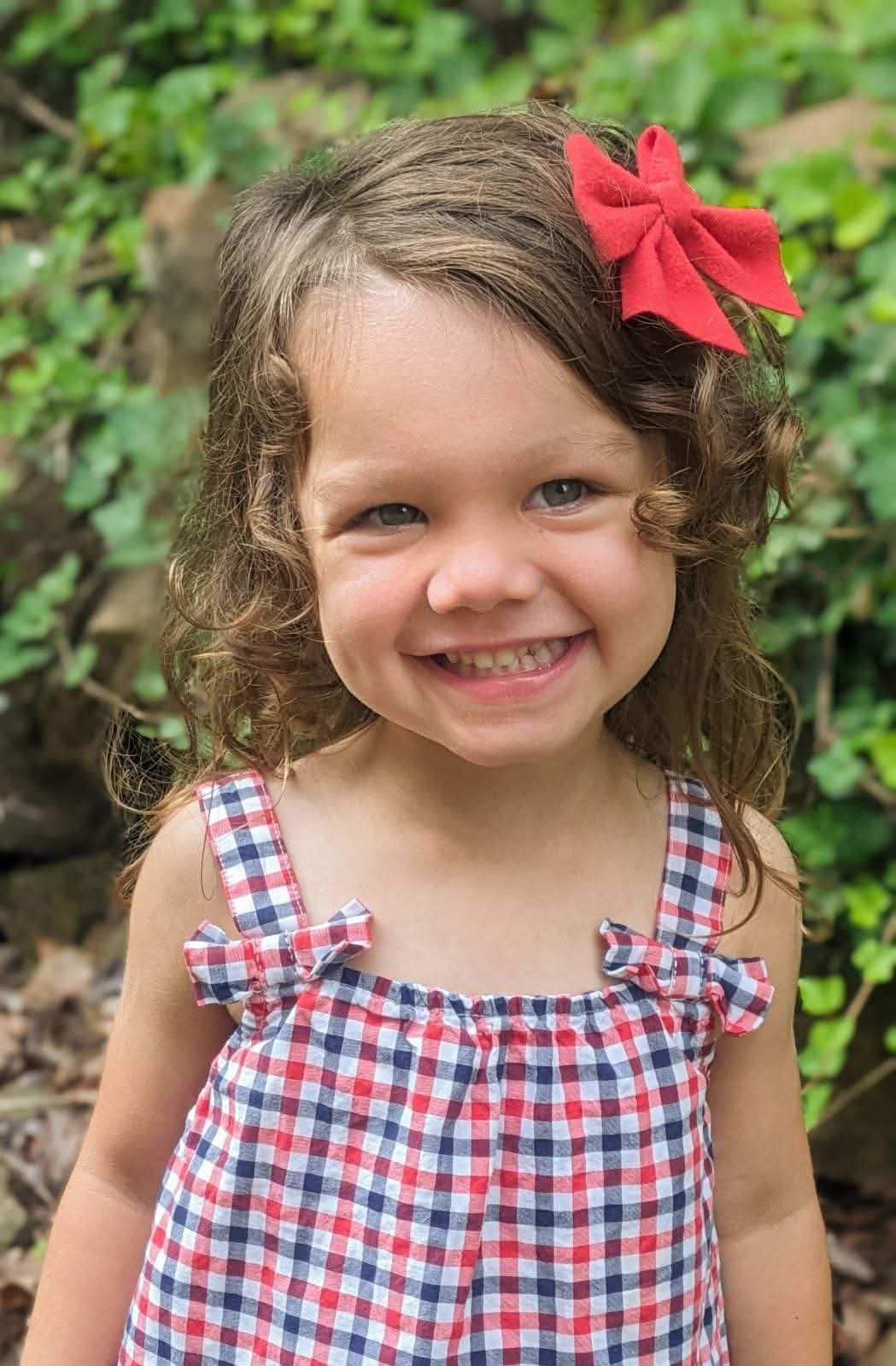 Girl in red gingham with a red bow, smiling