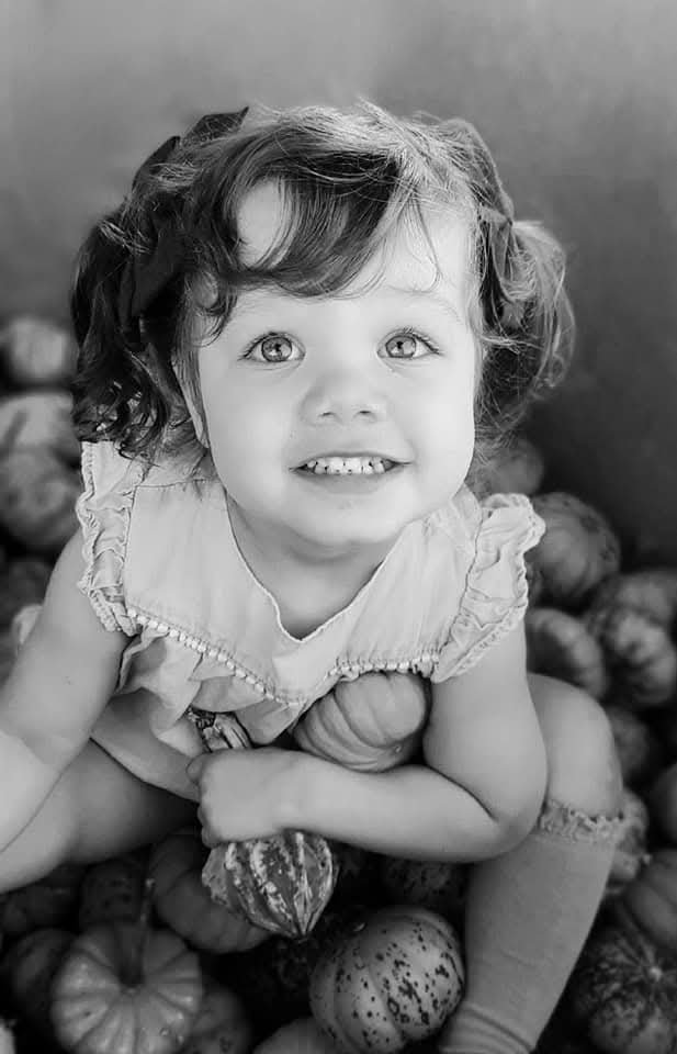 Toddler sitting among tiny pumpkins, black and white