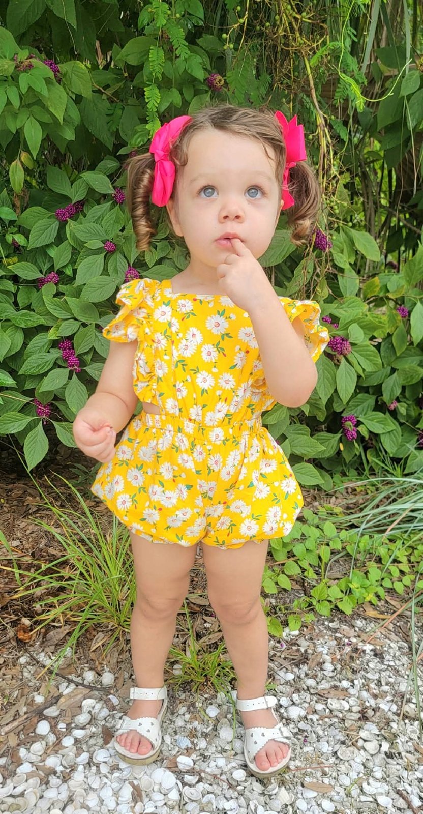Toddler in a yellow daisy romper with pink bows
