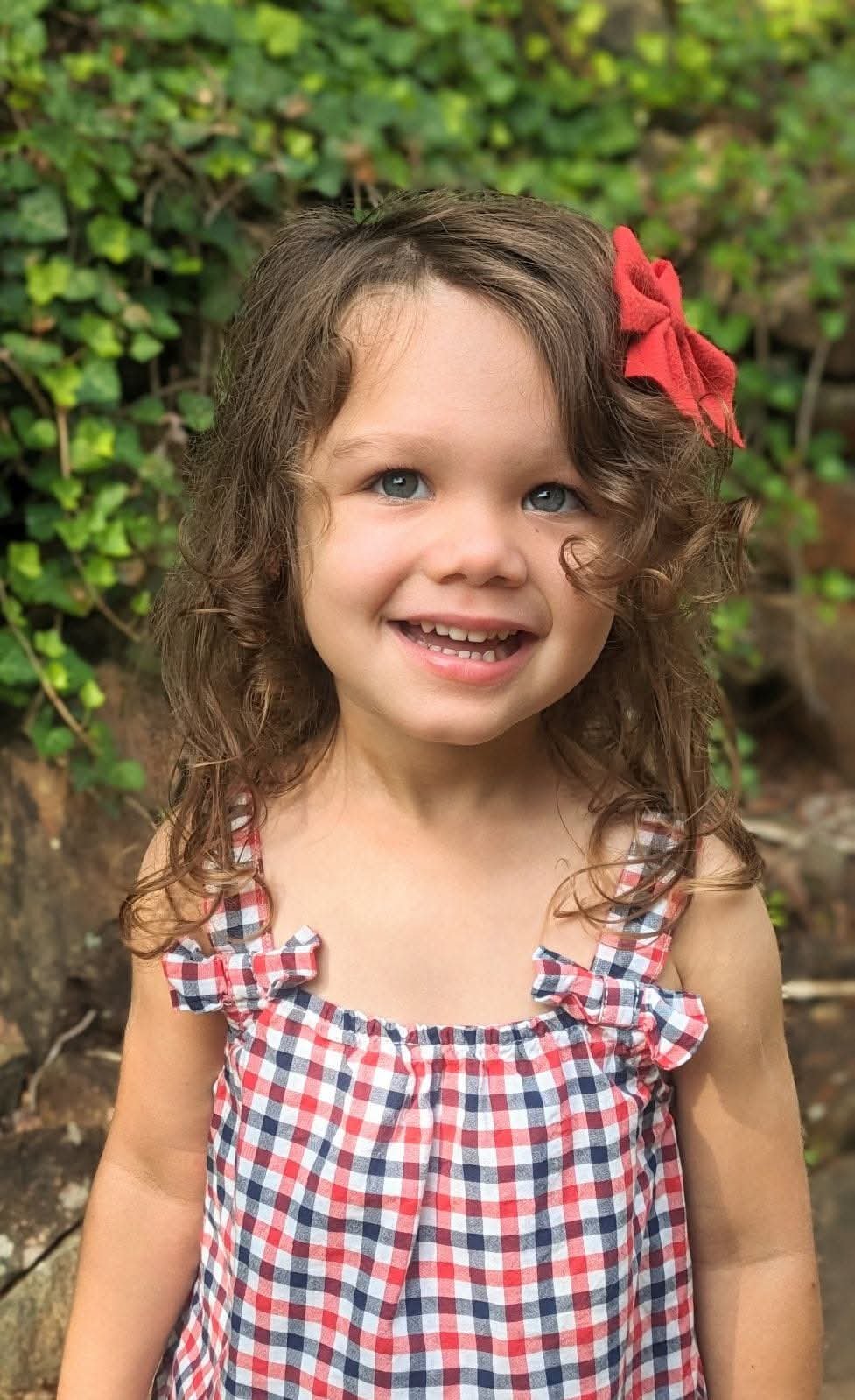 Girl in red gingham grinning by the ivy