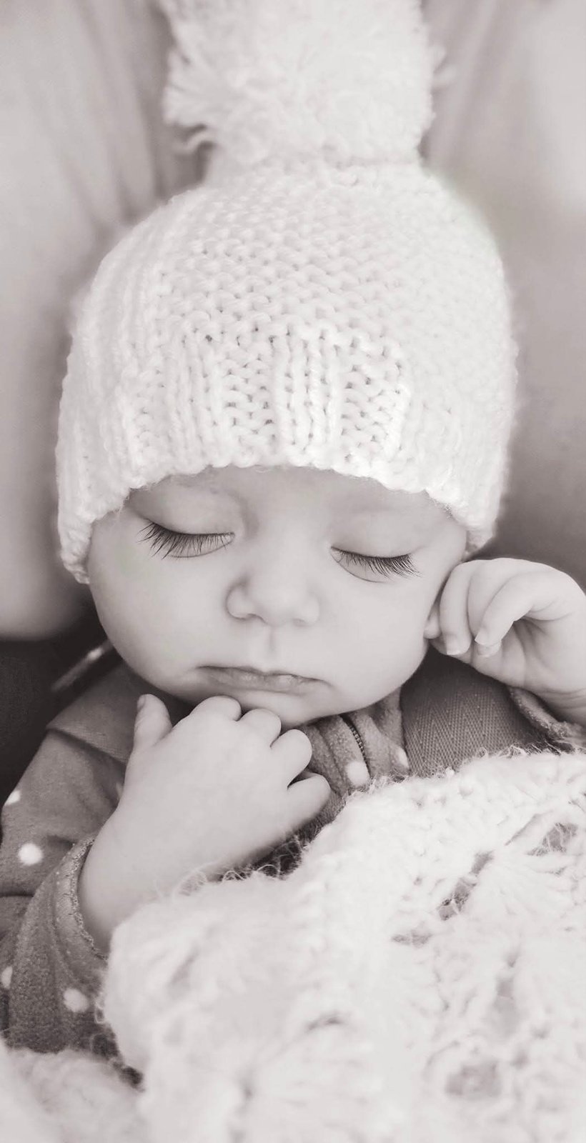 Baby sleeping in a pom-pom knit hat, black and white