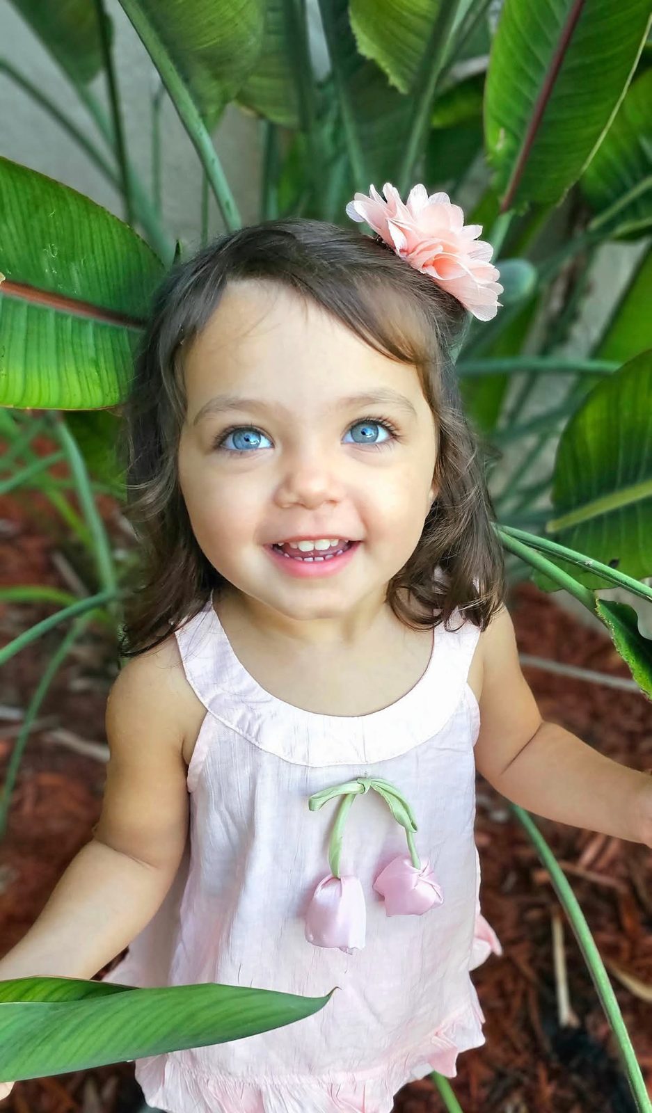 Toddler with a flower clip among banana leaves